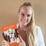 Smiling woman with long blonde hair in a light blazer holding an orange book titled JANNIS LOOTENS with white abstract shapes on the cover Danielle Joy Sawicka