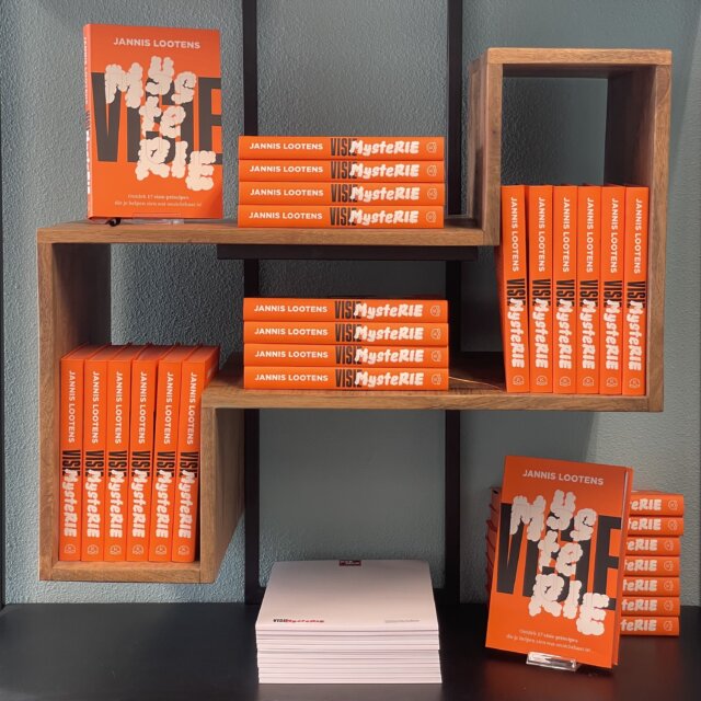 Orange book display Jannis Lootens titles stacked and lined on wooden shelves on a dark wall background Visie Mysterie Winkel display  Jannis Lootens